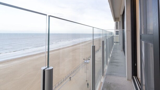 Un balcone con ringhiera in vetro che si affaccia su una spiaggia.