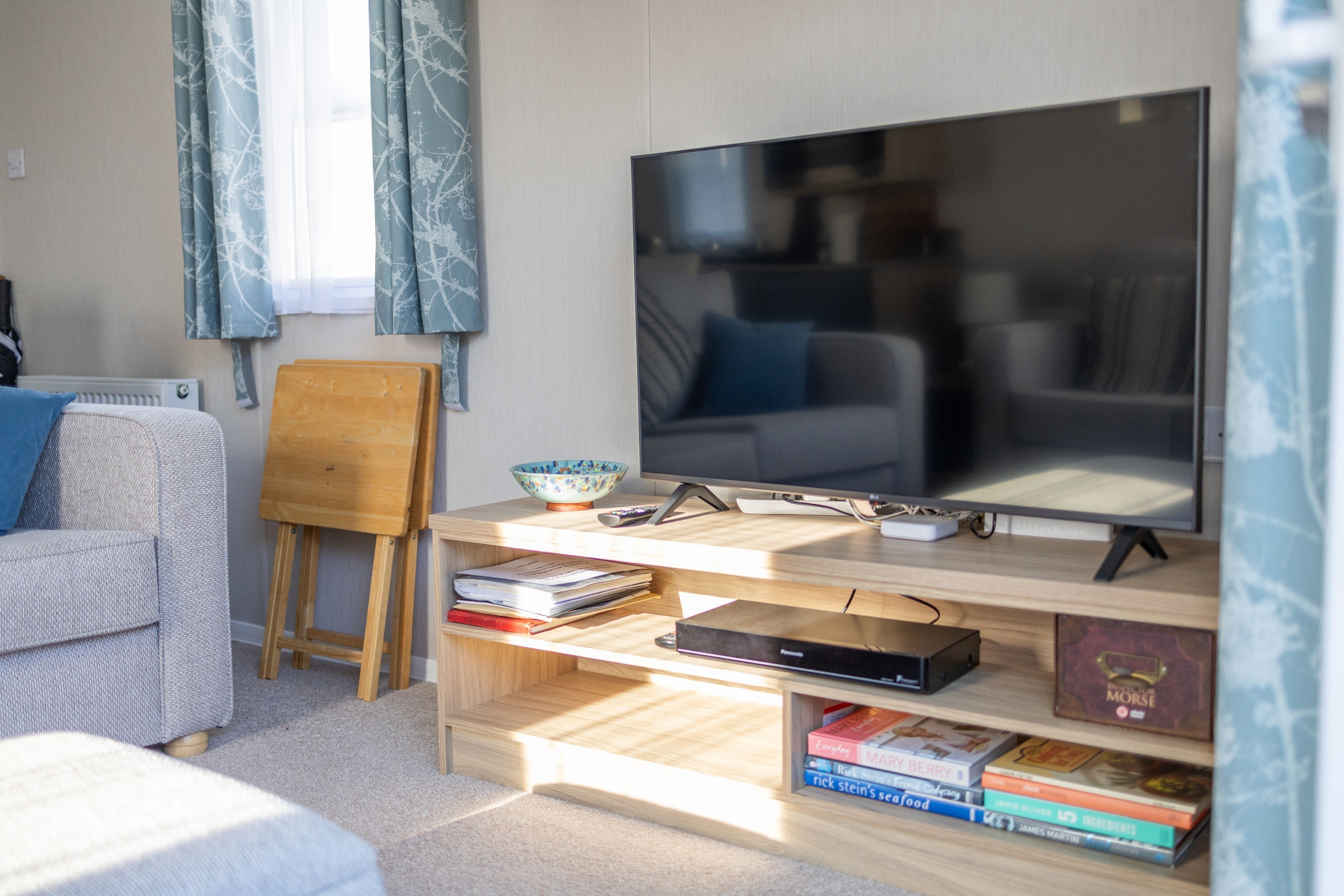 A living room with a flat-screen TV, wooden shelves, a small easel, and a bowl.