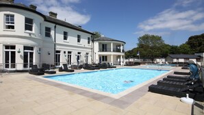 Una piscina con lettini e un edificio con diverse finestre e porte.