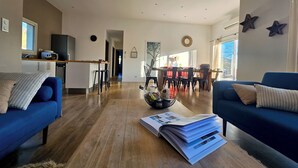 Una sala de estar moderna con un sofá azul, una mesa de centro con revistas y una cocina al fondo.