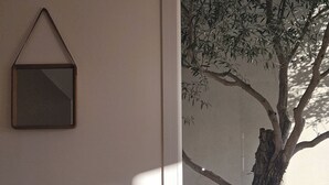 Una mesa de comedor con un plato y cubiertos, una silla, un cuadro en la pared y una ventana con vista a un árbol.
