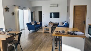 Una sala de estar moderna con piso de madera, un sofá azul, una mesa de comedor y un televisor montado en la pared.