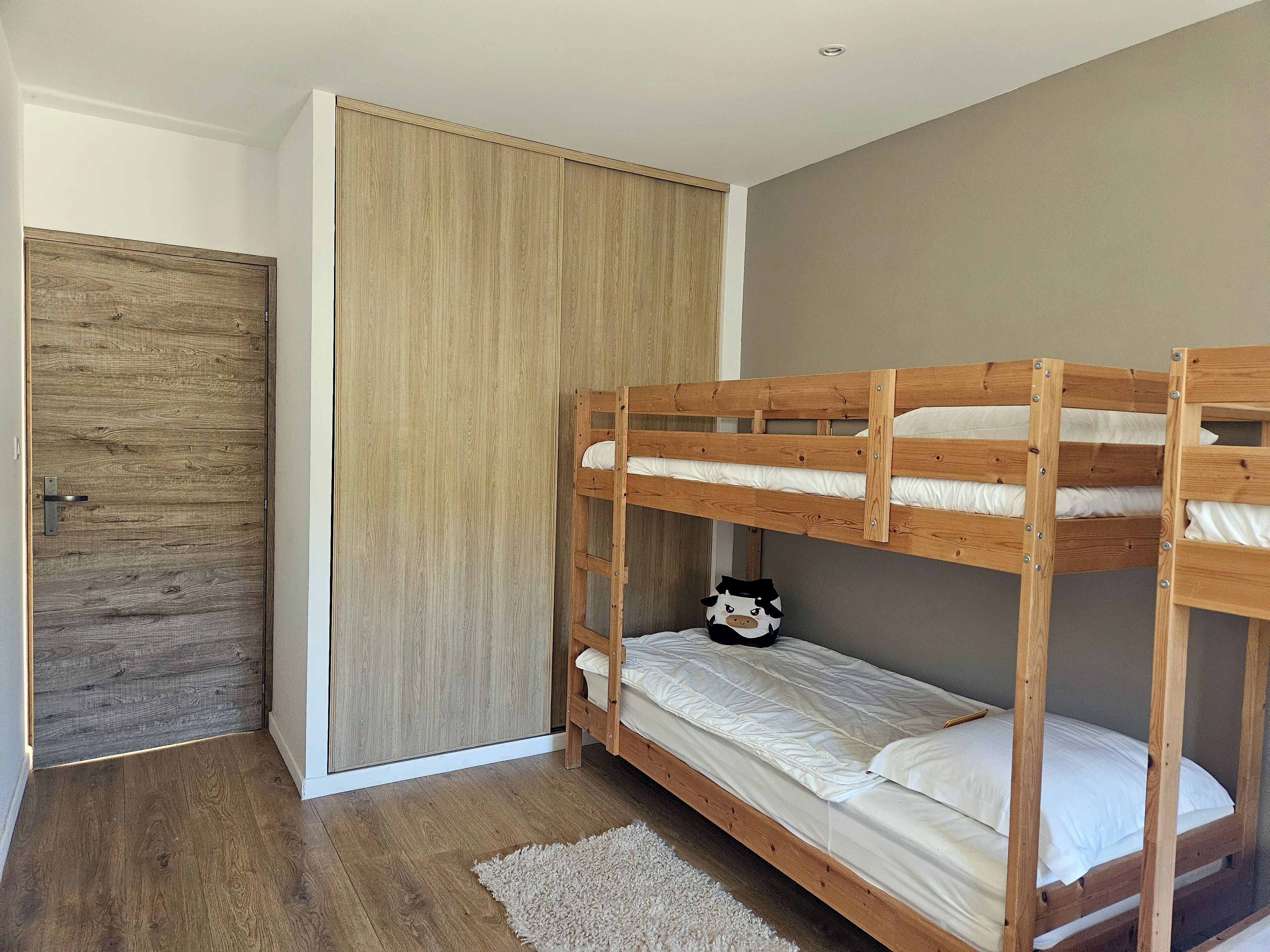 A bunk bed room with a wooden door, a wardrobe, and a small stuffed toy on the lower bunk.