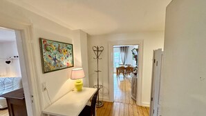 A room with a white table, a yellow lamp, a coat rack, and a painting on the wall.