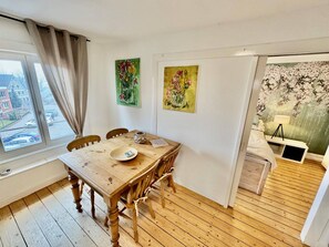 A dining area with a wooden table, chairs, a window with curtains, and two paintings on the wall. - Charmante Ferienwohnung in Geesthacht am Flussufer (Geesthacht)