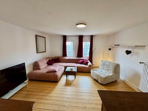 A living room with a sofa, a white armchair, a coffee table, and a TV. - Charmante Ferienwohnung in Geesthacht am Flussufer (Geesthacht)