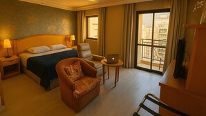 A hotel room with a bed, a chair, a desk with a laptop, and a TV. - Elegance Suítes Higienópolis (Sao Paulo)