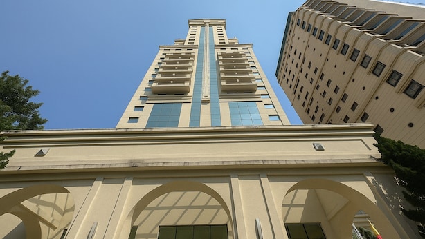 A tall building with a central vertical blue stripe, arched entryway, and a beige facade. - Elegance Suítes Higienópolis (Sao Paulo)