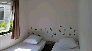 A room with two single beds, a window with curtains, and a wall decorated with butterfly decals. - Mobile home 300m from the beach (Saint-Hilaire-de-Riez)