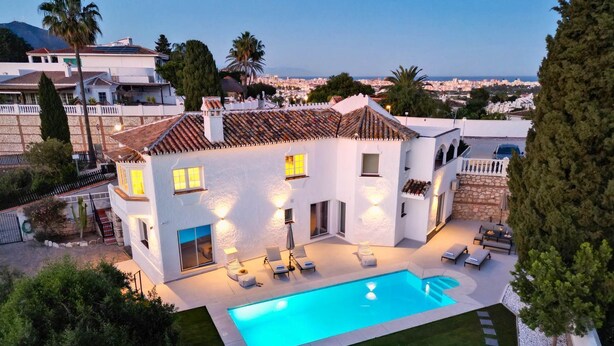 A modern villa with a swimming pool, outdoor seating, and a view of the city.