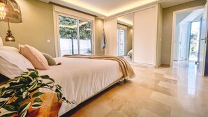 A spacious bedroom with a large bed, a potted plant, and a view of the outdoors through a sliding door.