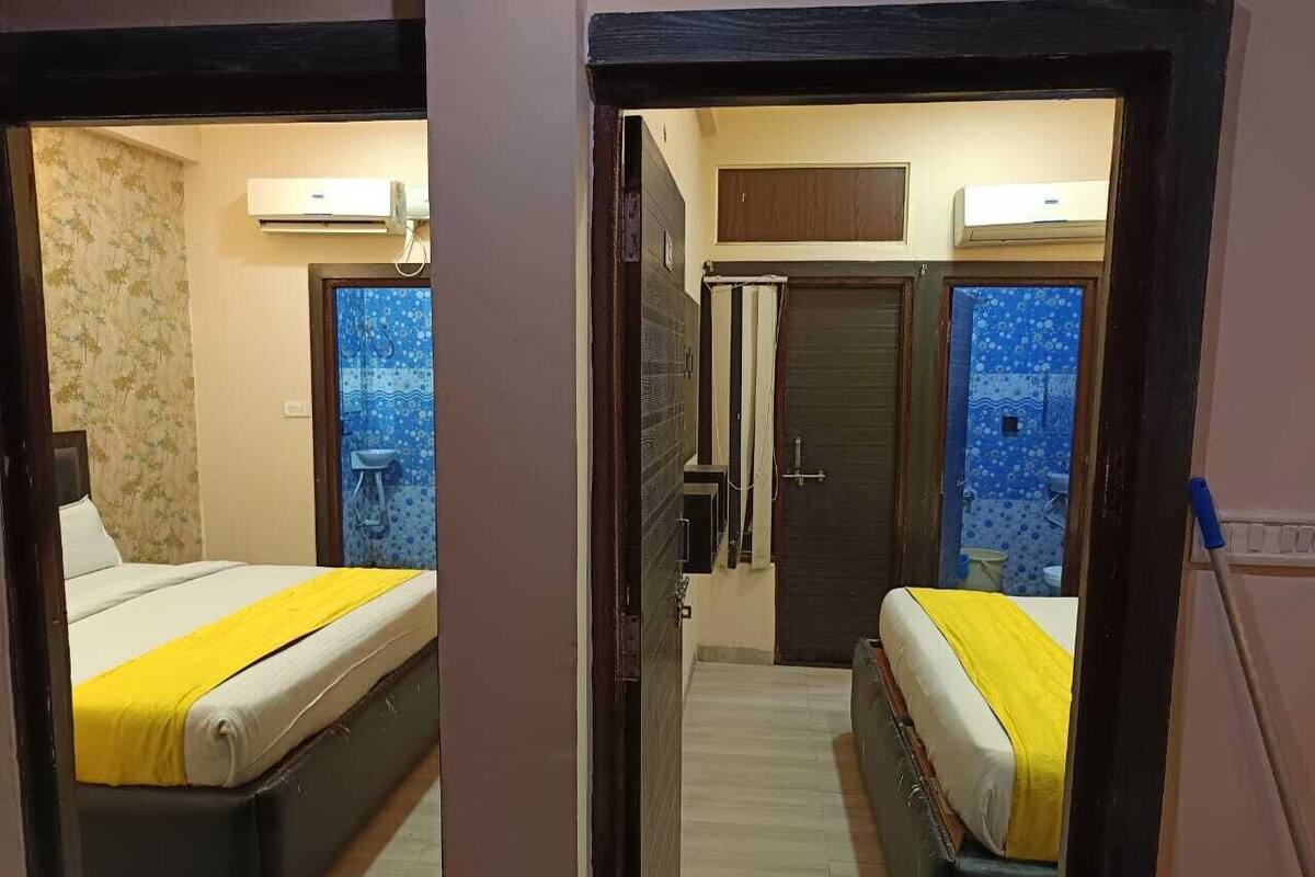 A hotel room with two beds, each with a yellow bedspread, a small window, and an air conditioning unit on the wall.