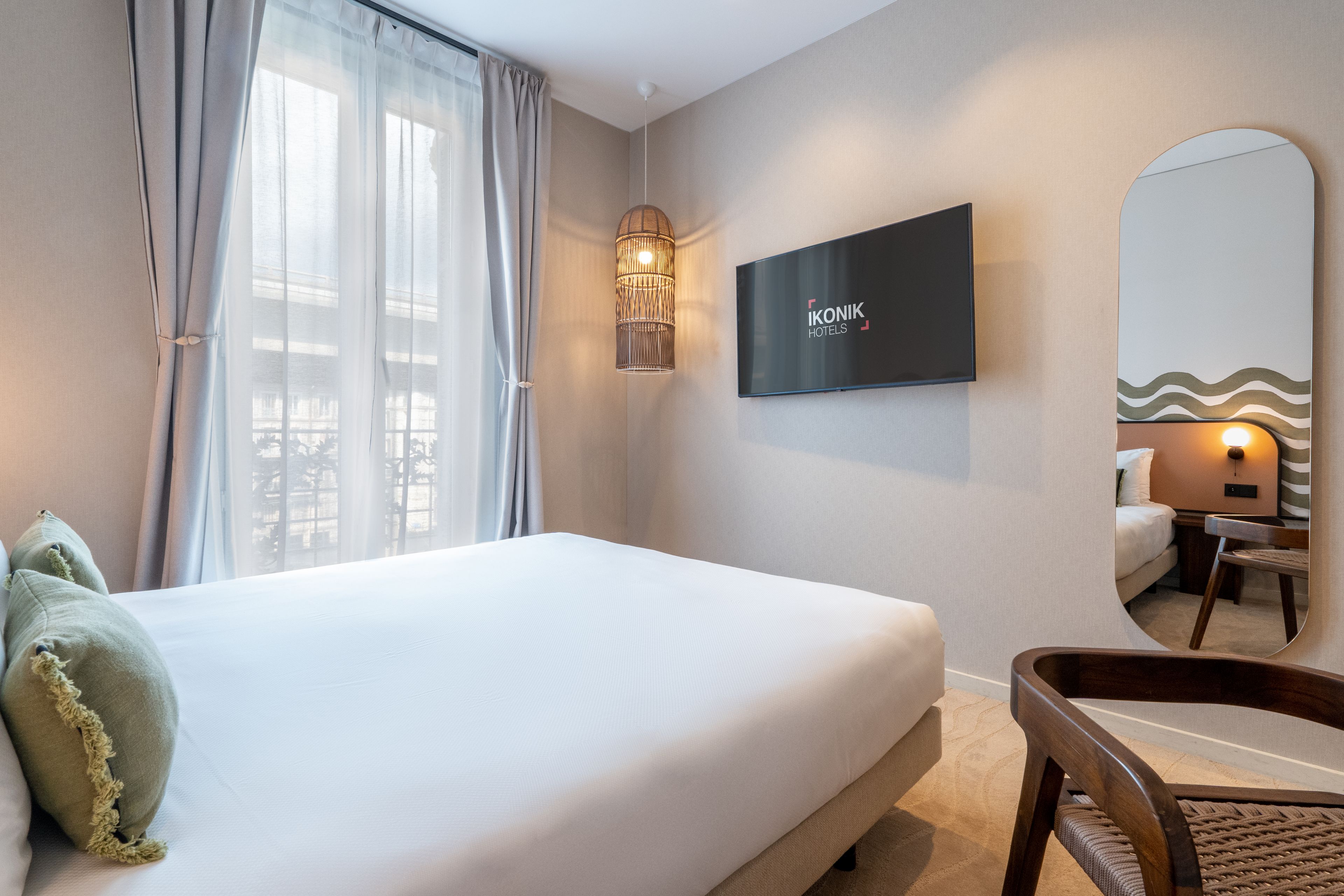 Una habitación de hotel con una cama, un televisor montado en la pared y un espejo grande.