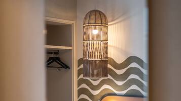 A hotel room with a bed, a hanging light fixture, a wardrobe, and a patterned wall.