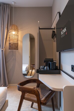 Ein modernes Hotelzimmer mit Bett, Schreibtisch mit Kaffeemaschine, Spiegel und Pendelleuchte.