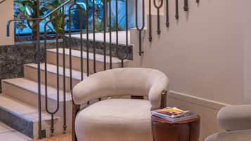 Un interior moderno con una escalera, un sillón acolchado y una pequeña mesa con libros.