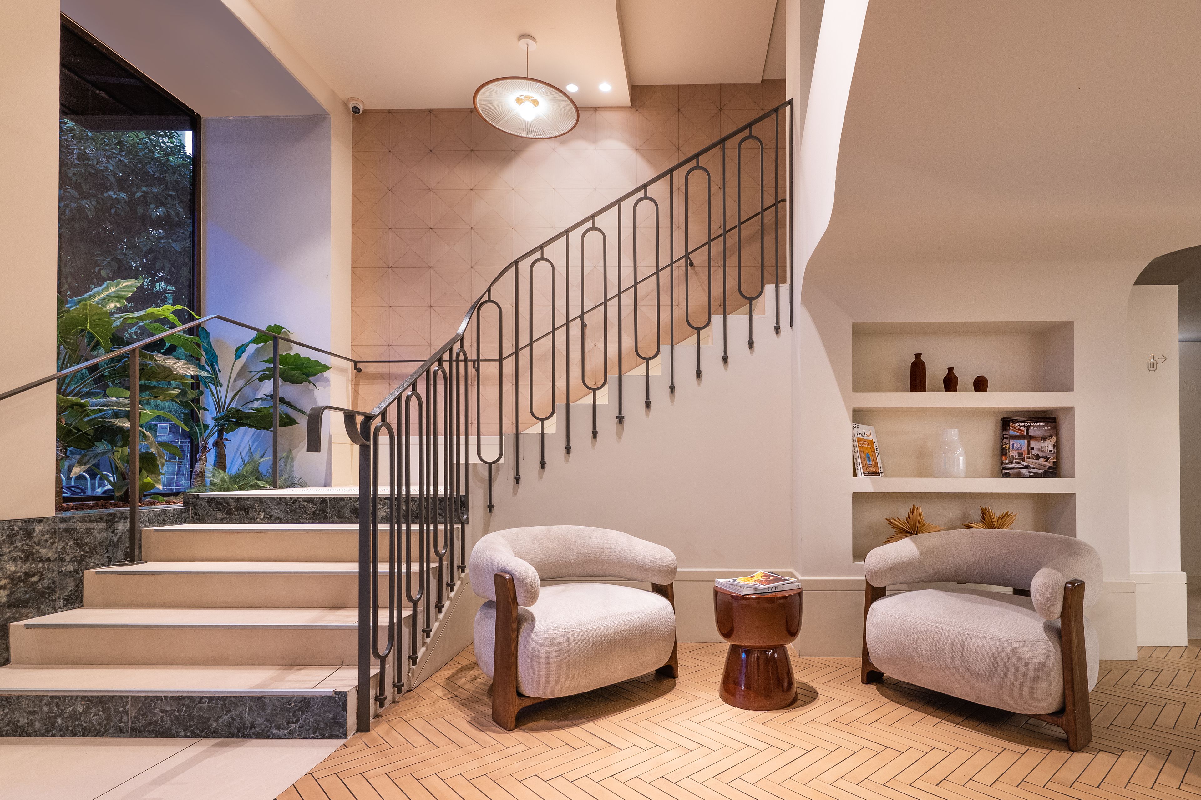 Un interior moderno con una escalera, dos sillones, una mesa de centro y una estantería.