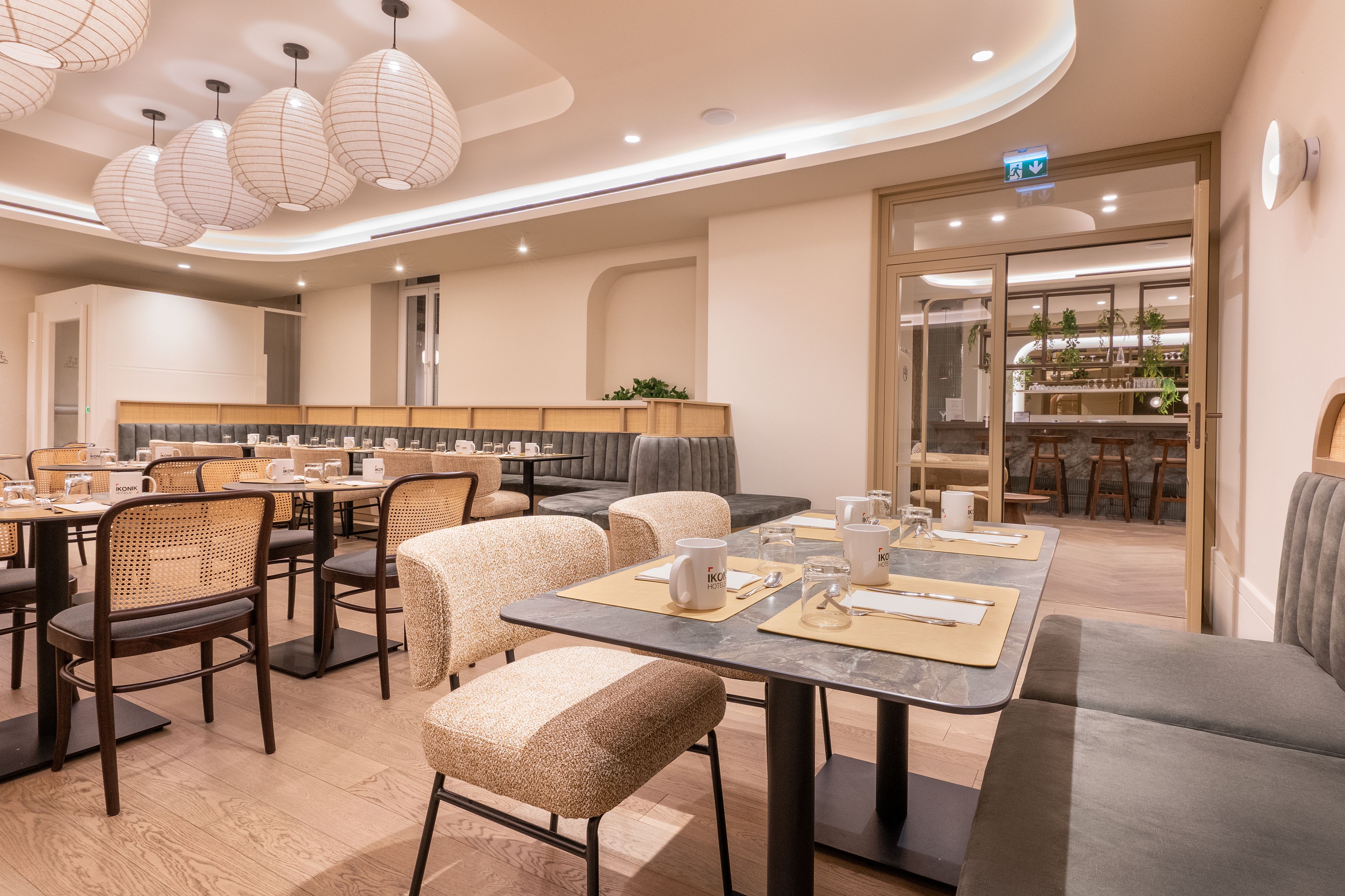 Un área de comedor de hotel moderna con mesas redondas, sillas acolchadas e iluminación colgante.