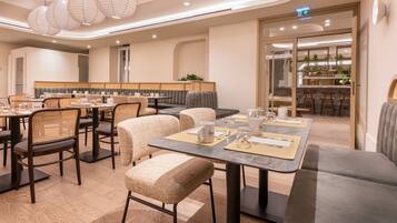 Un área de comedor de hotel moderna con mesas redondas, sillas acolchadas e iluminación colgante.