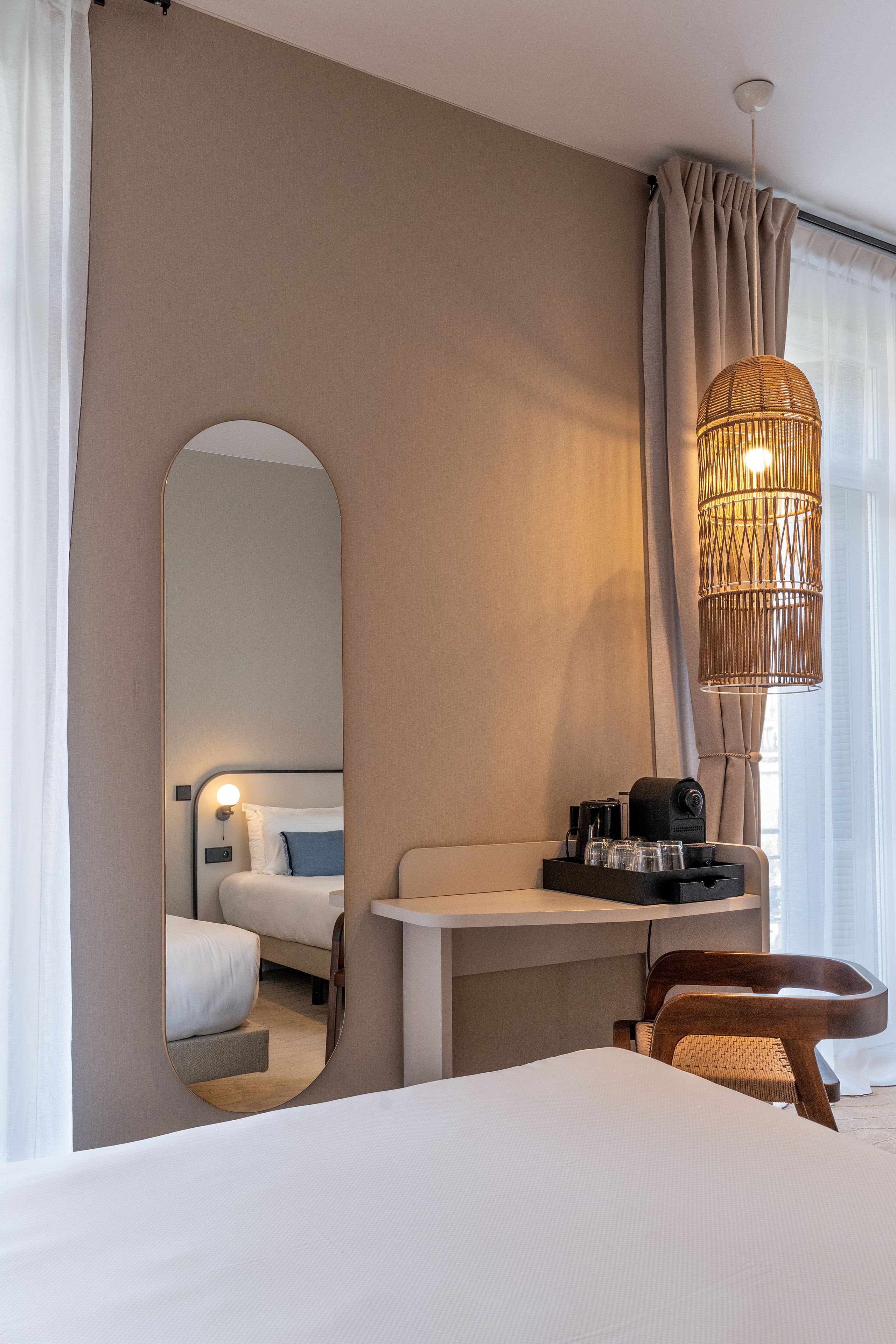 Una habitación de hotel con cama, escritorio con cafetera, una silla y una lámpara colgante.