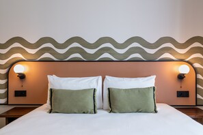 A bed with two pillows, a headboard with a wavy pattern, and wall-mounted lights. -  Ikonik Marengo (Nice)