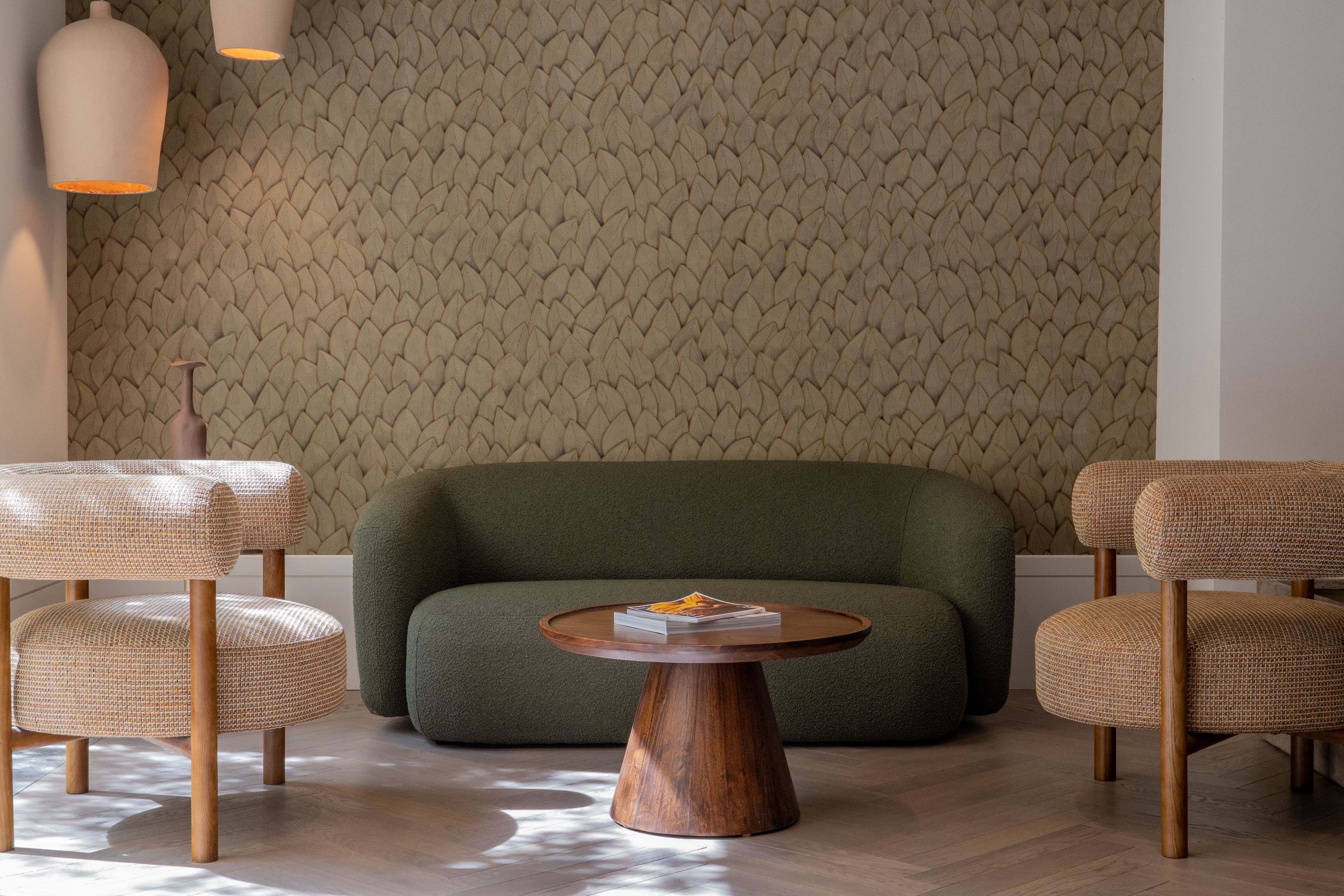 A room with a patterned wallpaper, a green sofa, and wicker chairs.