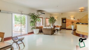 Un vestíbulo amplio con una recepción, muebles de mimbre, plantas en macetas y vistas a un área exterior a través de puertas de cristal.