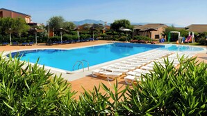 Una piscina con sillas de descanso y un tobogán, rodeada de vegetación y edificios.