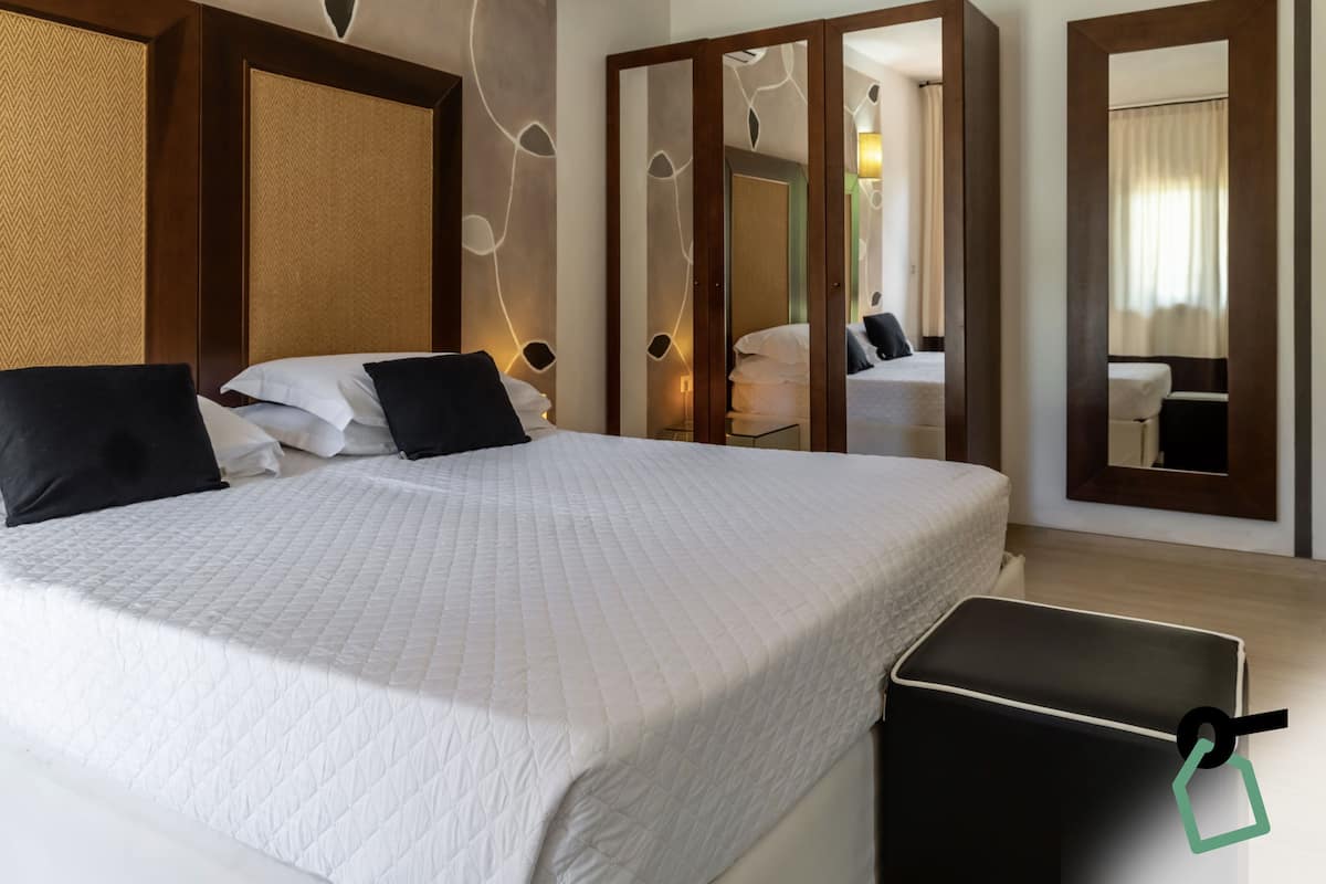 A hotel room with a large bed, a bedside table, a mirror, and a wardrobe.