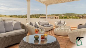 Una terraza en la azotea con mobiliario de mimbre, una mesa de cristal y vistas del paisaje circundante.