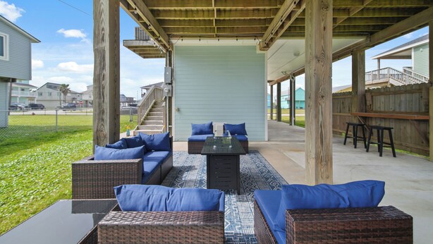 An outdoor patio with wicker furniture and blue cushions, a covered area with a wooden ceiling, and a view of neighboring houses. - Twins Tidal Escape, Sweet Memories, S'More Fun (Galveston)