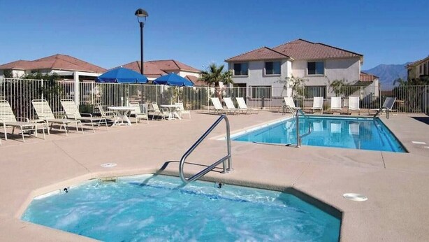 A pool area with lounge chairs and umbrellas, a small hot tub, and a building with a tiled roof.