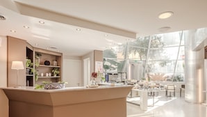 Un hall d’hôtel moderne doté d’un comptoir d’accueil, d’un espace salon et de grandes fenêtres offrant une vue sur l’extérieur.