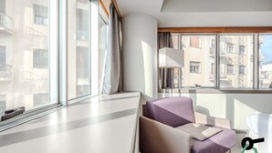 Une chambre d’hôtel moderne avec une grande fenêtre, un canapé, une table de chevet et une lampe.
