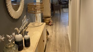 A modern living room with a wooden floor, a large mirror, a wicker lamp, and a bookshelf.