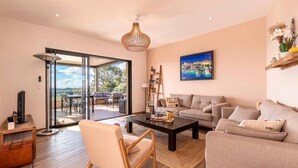 A modern living room with a sofa, armchairs, a coffee table, and a TV. There is a large window with a view of the outdoors. - 150m2 4 bedroom family home located in San gavino 10min from figari (Figari)
