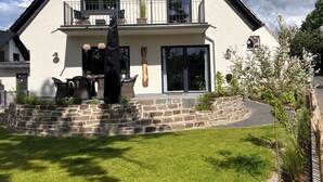 Een huis met twee verdiepingen, een stenen fundering, een balkon met tuinmeubilair en een verzorgd gazon.