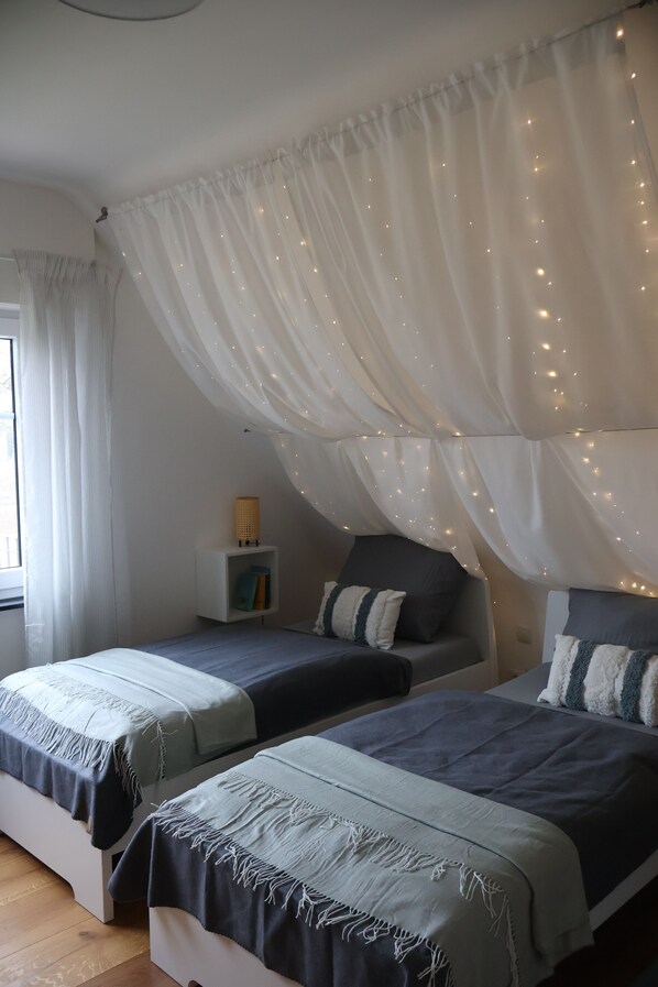 Une chambre avec deux lits, une table de chevet avec une lampe et une fenêtre avec des rideaux.