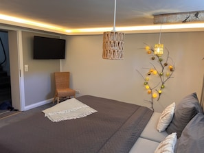 Une chambre à coucher comprenant un lit, une chaise, un téléviseur, un luminaire fixé au mur et une branche décorative illuminée.