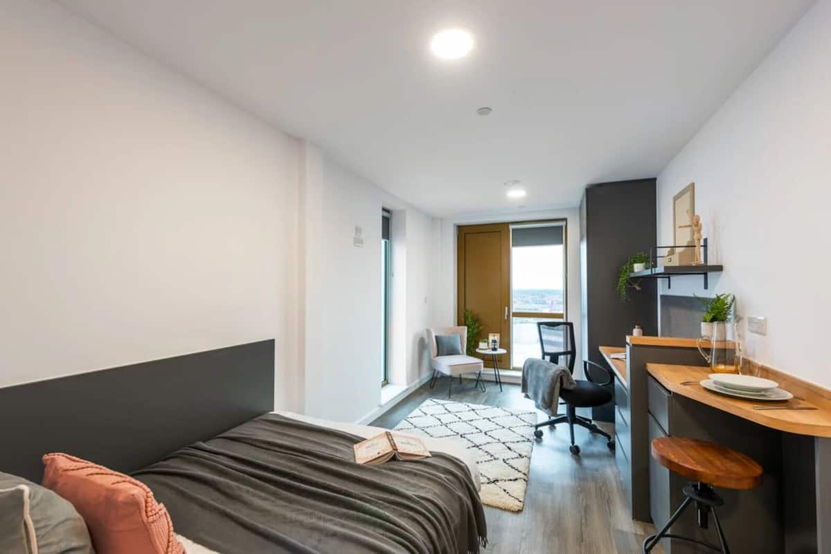 Habitació d'hotel moderna i compacta amb llit, escriptori i petita cuineta.