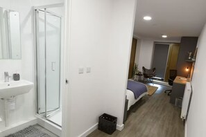 A modern hotel room with a shower, sink, bed, desk, and chair.
