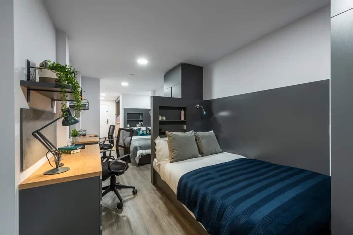 Un dormitori modern amb llit, escriptori, cadira i una petita zona d'oficina.