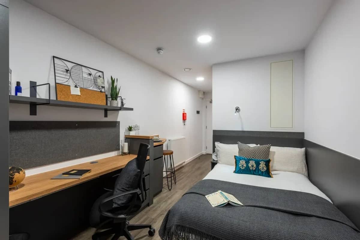 Habitació d'hotel moderna amb escriptori, cadira i llit amb almofadons decoratius.