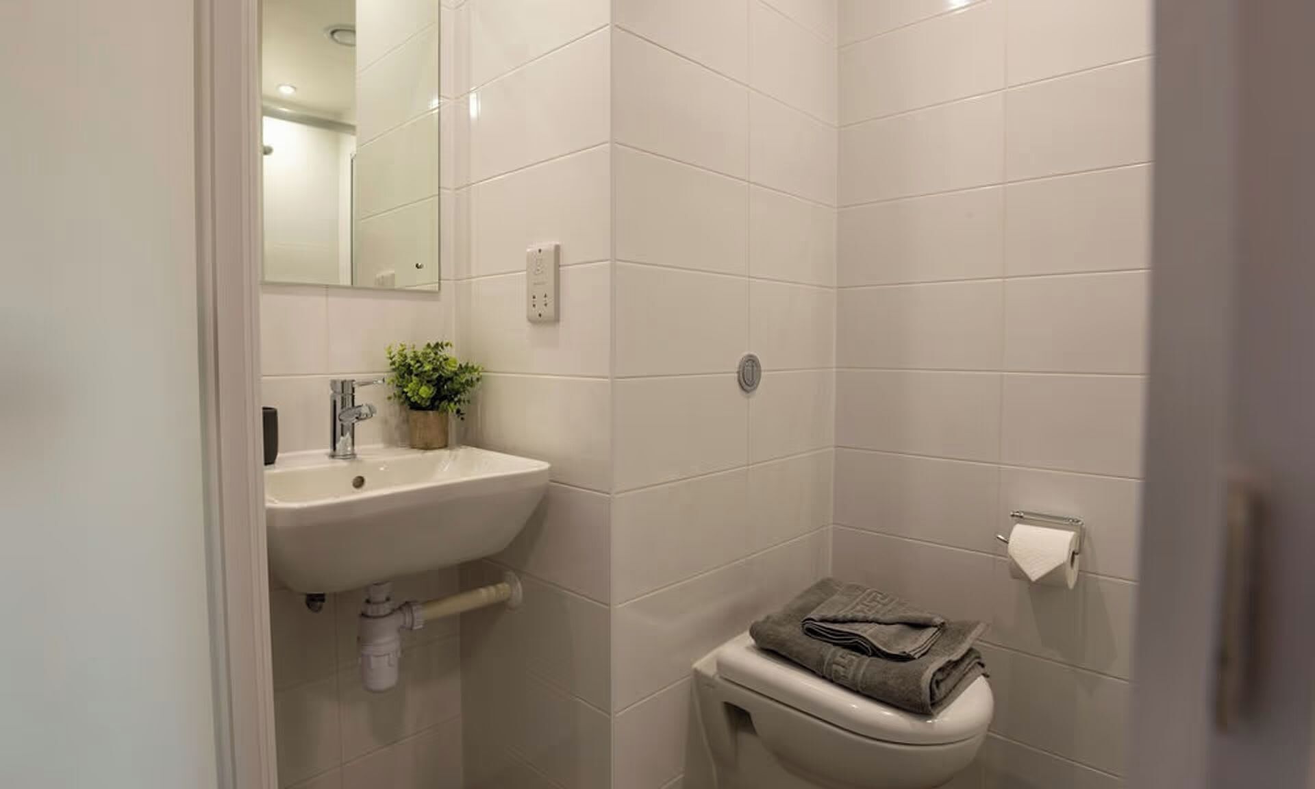 A bathroom with a sink, mirror, toilet, and a towel on the toilet.