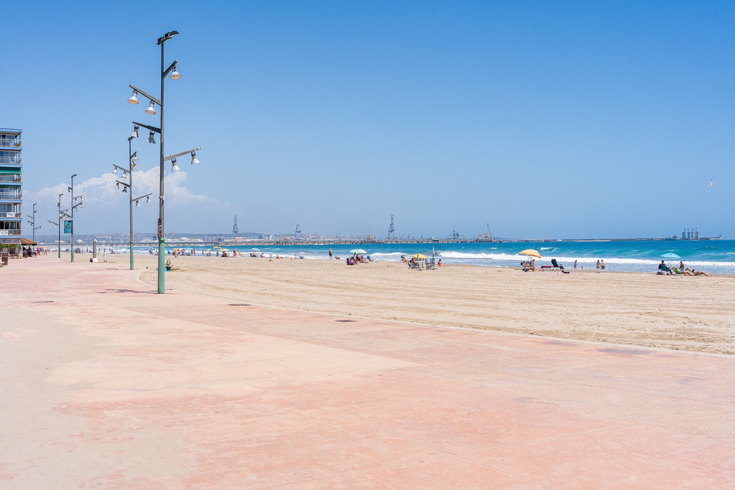 A beach with a wide promenade, street lamps, and a clear view of the ocean.