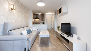 Una sala moderna con un sofá, una mesa de centro, un televisor y una cocina al fondo.