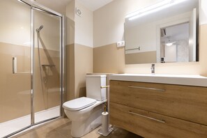 A modern bathroom with a glass shower enclosure, a white toilet, and wooden cabinetry. - TECAVI II Apartment (La Pineda)