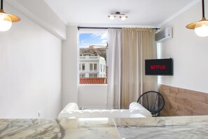 A modern hotel room with a marble-topped bed, a black chair, a television mounted on the wall, and a view of a building through a window with beige curtains. - Monastiraki 507 Superhost Hub (Athens)