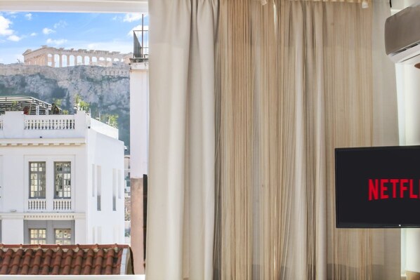 Habitación con vista a un edificio blanco con balcones y una montaña al fondo. Una pantalla de televisión muestra el logotipo de Netflix.