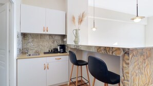 A modern kitchen with white cabinets, a marble backsplash, and two black bar stools. - Monastiraki 507 Superhost Hub (Athens)